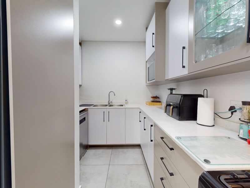 A modern, well-maintained scullery featuring clean white cabinetry, stone countertops, a double sink, and tiled flooring, providing efficient additional kitchen workspace.