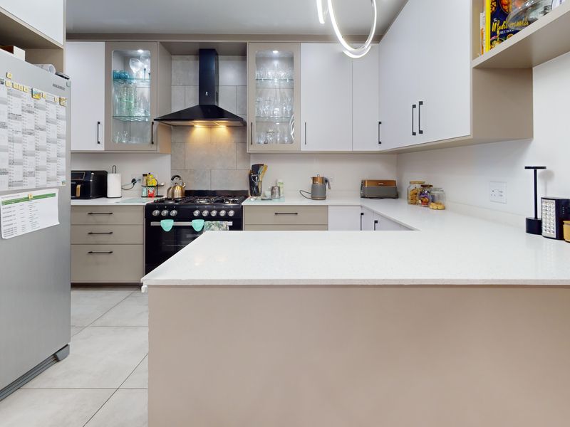 Modern kitchen featuring sleek white and neutral cabinetry, quartz countertops, a gas stove with extractor fan, and contemporary tiled finishes.