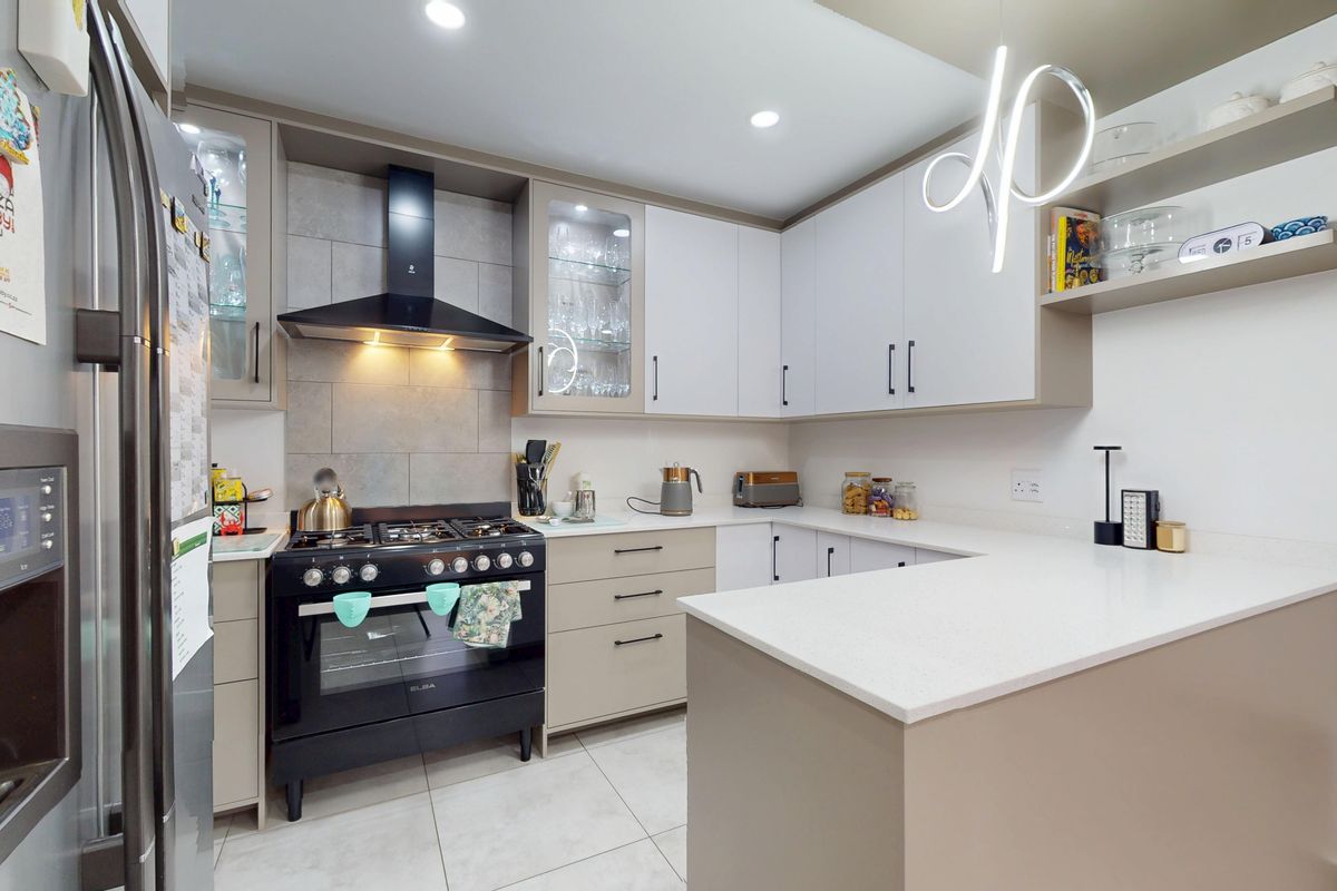 A modern, well-maintained kitchen featuring sleek cabinetry, quartz countertops, a gas stove with extractor fan, and contemporary recessed lighting.