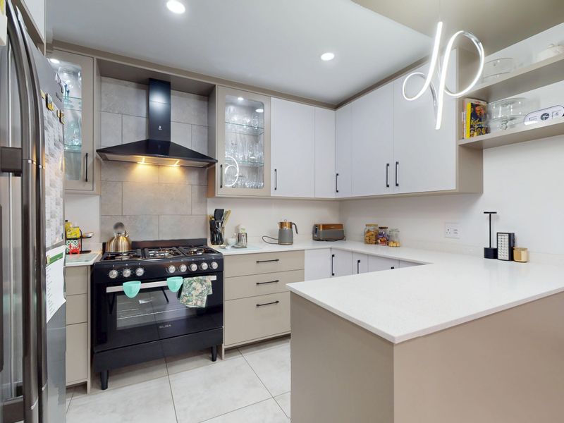 A modern, well-maintained kitchen featuring sleek cabinetry, quartz countertops, a gas stove with extractor fan, and contemporary recessed lighting.