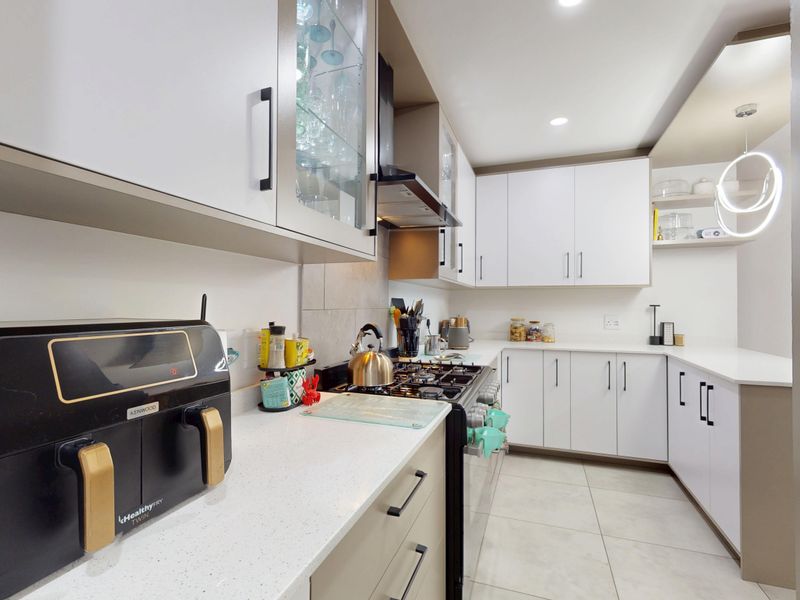 Modern kitchen featuring white cabinetry, quartz countertops, a gas hob with extractor fan, and neutral tiled flooring.