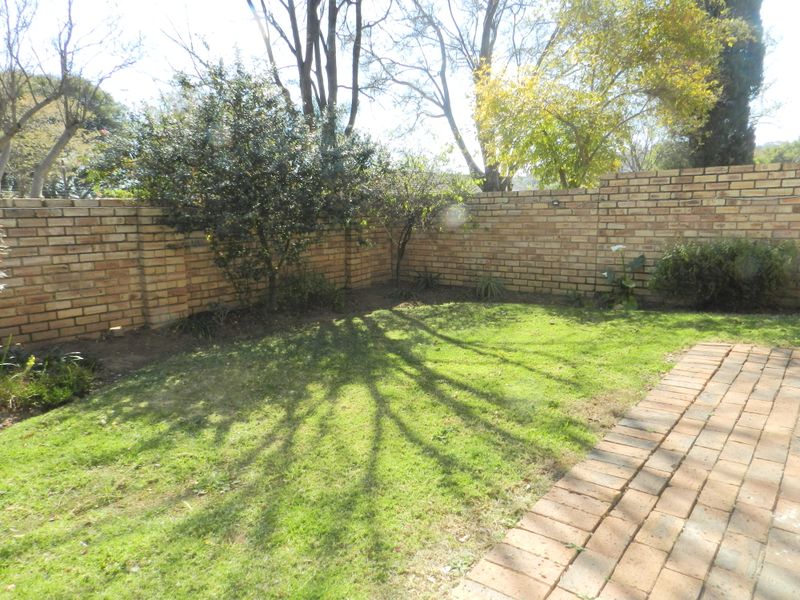 A private rear garden featuring a well-maintained lawn, established trees, and a brick boundary wall with a paved walkway.