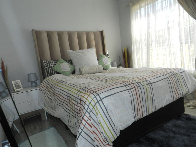 A well-lit bedroom featuring neutral wall tones, laminate flooring, and large windows with sheer curtains, providing a comfortable and bright living space.