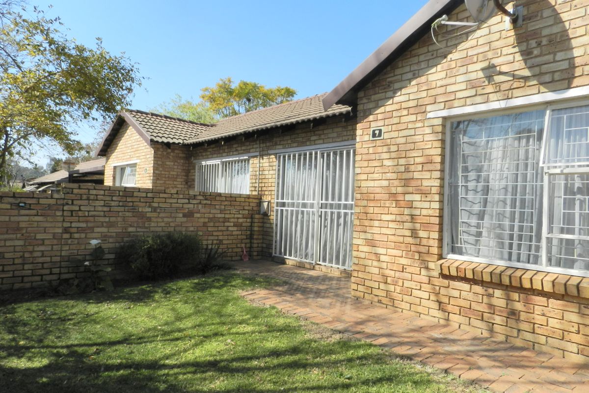 Rear view of a face brick townhouse featuring a small private garden, paved walkway, and secure sliding door access.