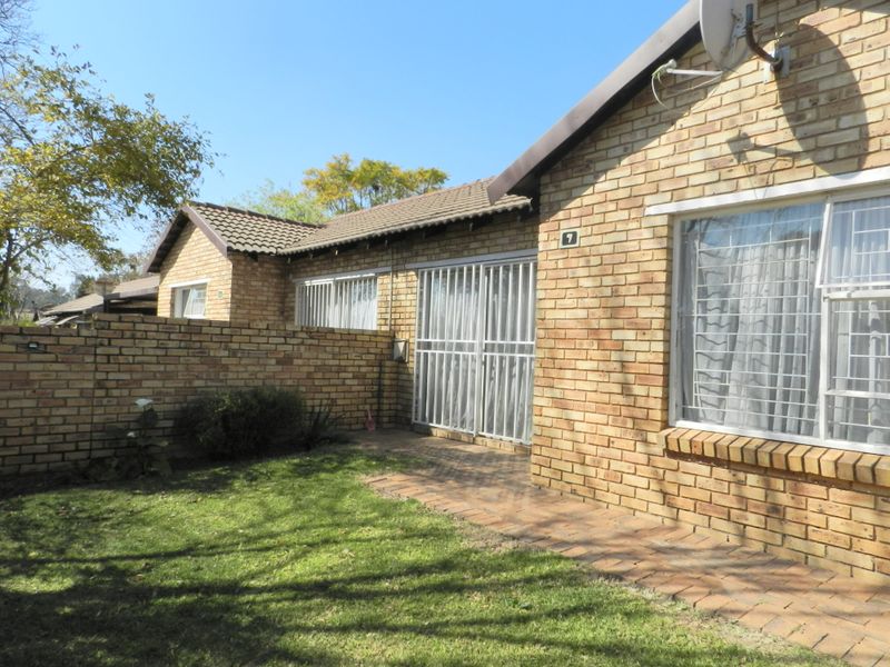 Rear view of a face brick townhouse featuring a small private garden, paved walkway, and secure sliding door access.