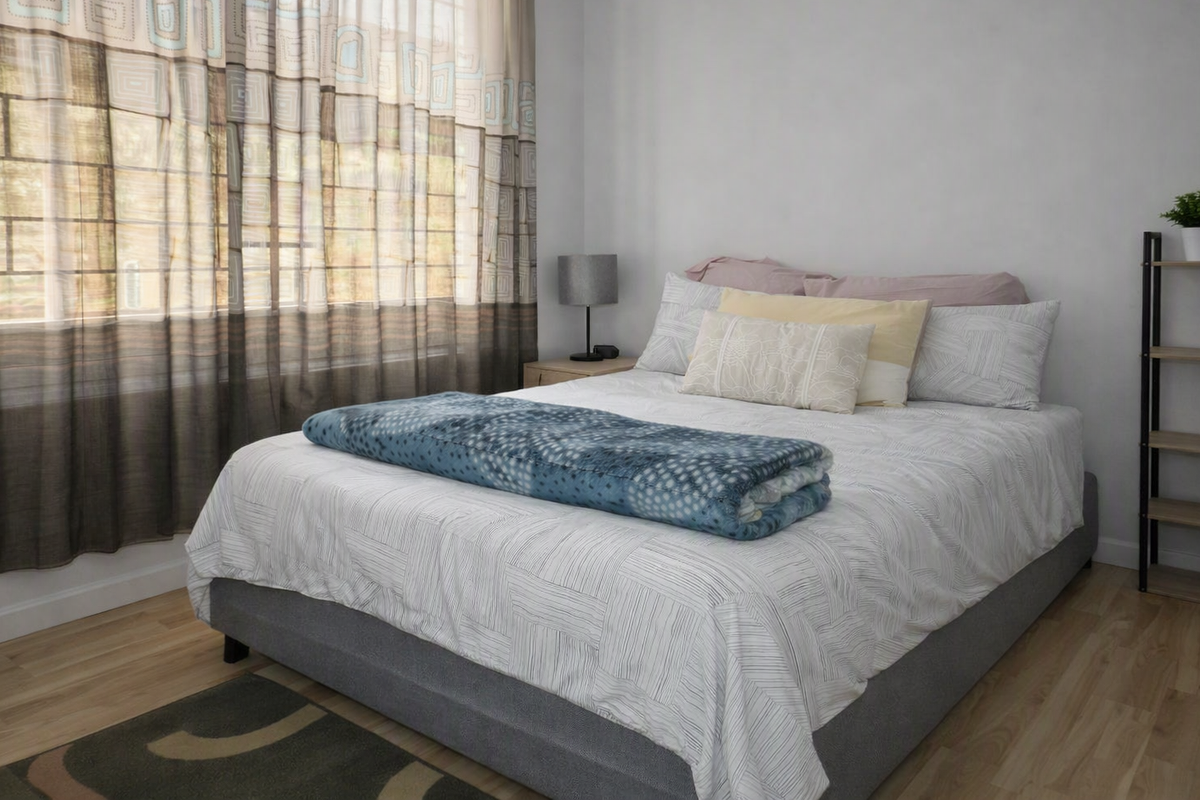 A well-lit bedroom featuring light-toned laminate flooring and large windows with installed curtain tracks, providing a neutral and comfortable living space.