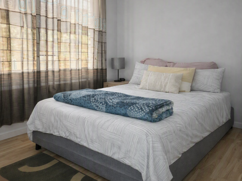 A well-lit bedroom featuring light-toned laminate flooring and large windows with installed curtain tracks, providing a neutral and comfortable living space.