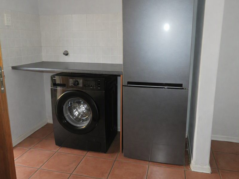 A functional laundry area featuring tiled flooring, a tiled splashback, and a laminate countertop with dedicated plumbing connections for appliances.