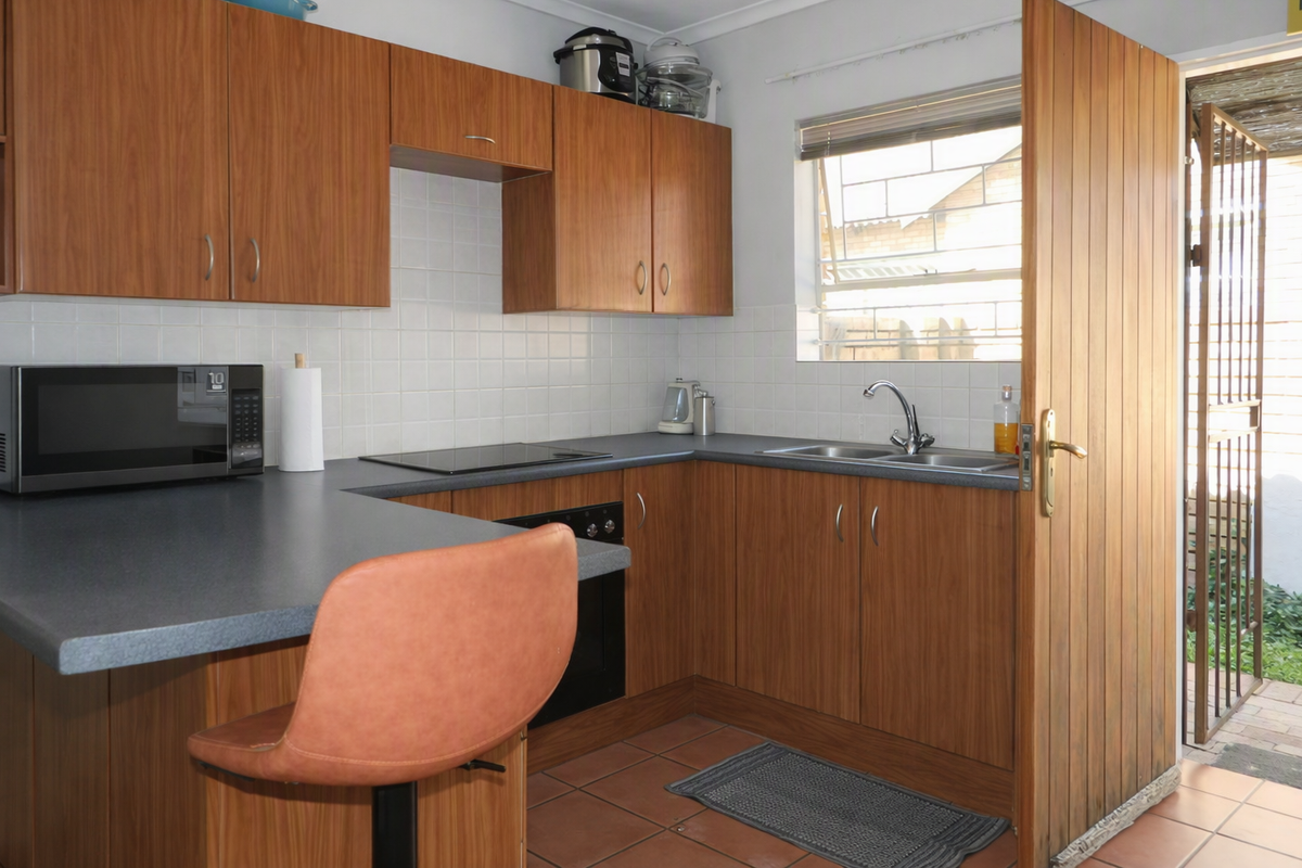 Functional kitchen featuring wood-look cabinetry, dark countertops, built-in oven and hob, tiled backsplash, and direct access to the exterior via a security gate.