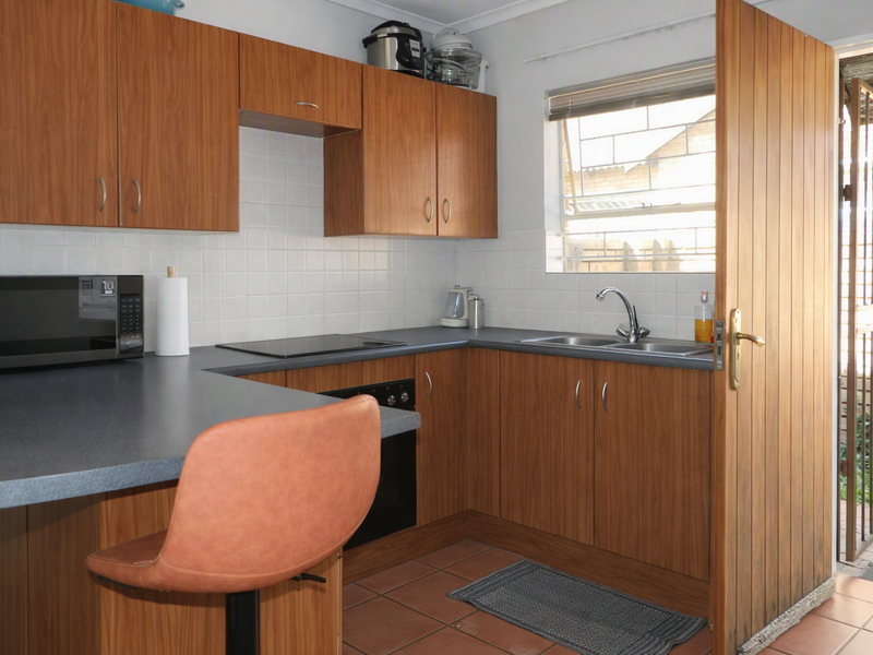 Functional kitchen featuring wood-look cabinetry, dark countertops, built-in oven and hob, tiled backsplash, and direct access to the exterior via a security gate.