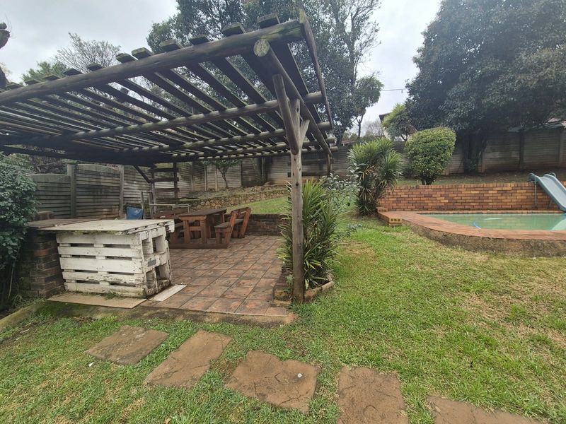 Outdoor entertainment area featuring a wooden pergola, tiled patio, and a swimming pool with brick retaining walls in a garden setting.