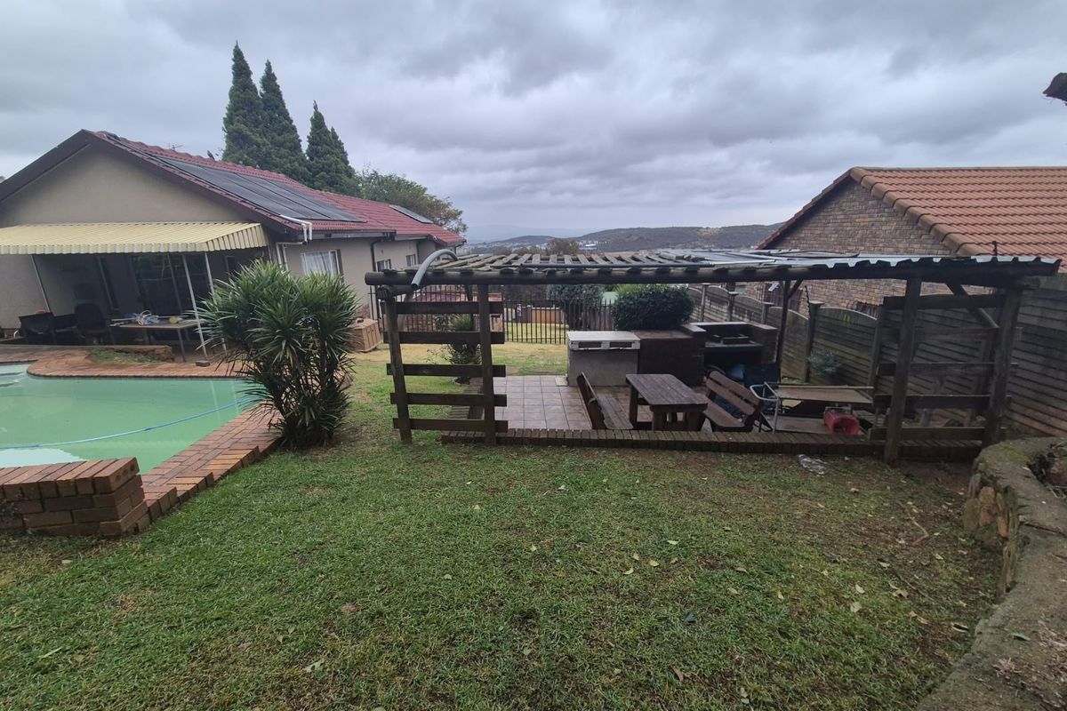 Rear garden featuring a swimming pool, a timber pergola with a built-in braai area, and views of the surrounding landscape.