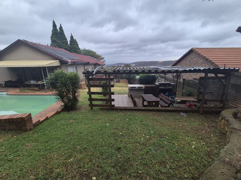 Rear garden featuring a swimming pool, a timber pergola with a built-in braai area, and views of the surrounding landscape.