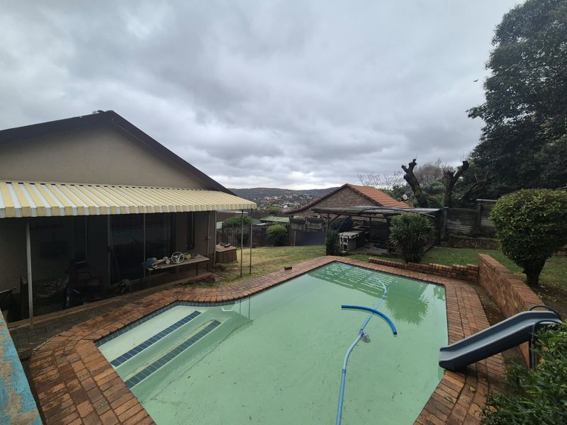 Outdoor pool area featuring a swimming pool with brick coping, a slide, and an attached covered patio with a retractable awning.