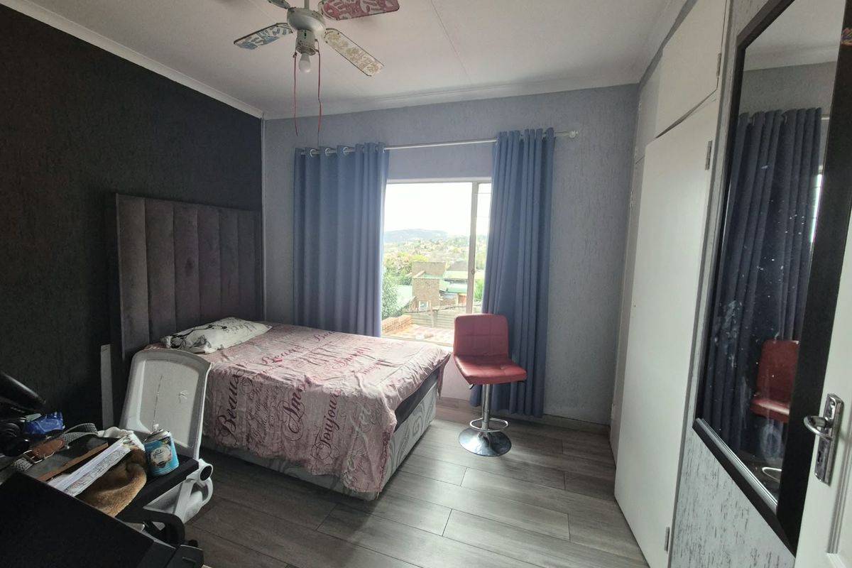 A bedroom featuring laminate flooring, built-in cupboards, and a ceiling fan, with a window offering an elevated view.