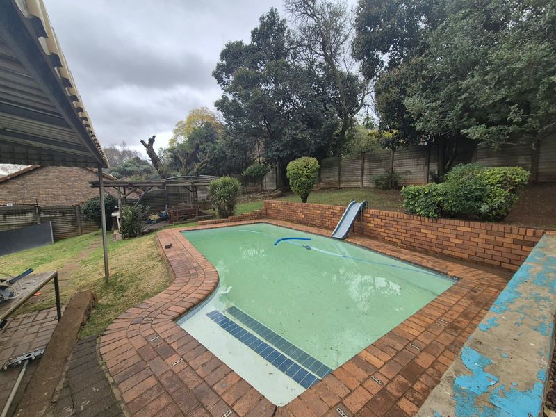 Outdoor pool area featuring a brick-lined swimming pool, retaining walls, and surrounding garden space, requiring maintenance and pool water treatment.