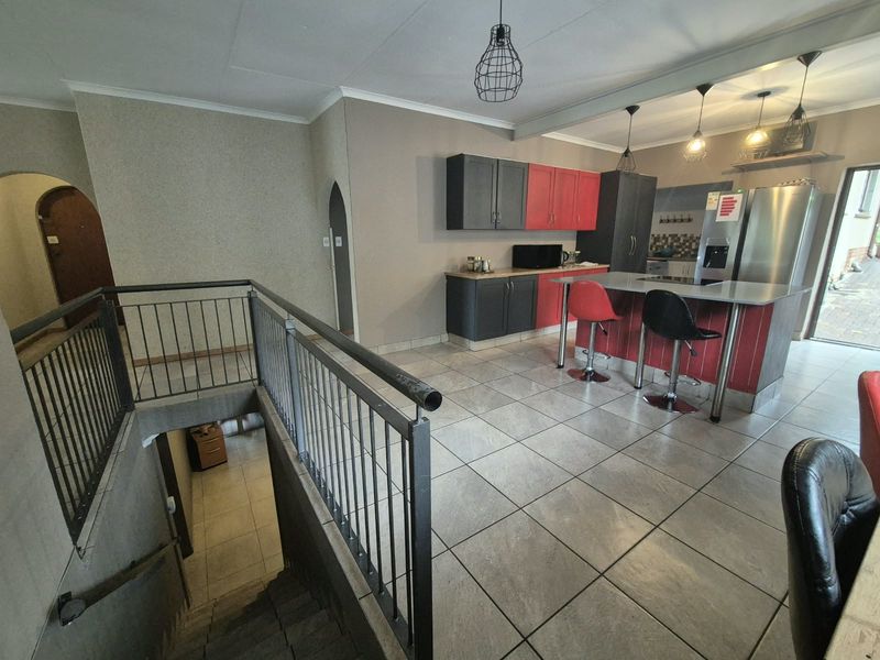 Open plan kitchen area featuring a central island, tiled flooring, and a staircase with a metal balustrade leading to the lower level.