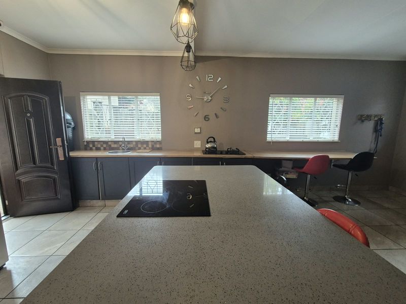 Modern kitchen featuring a large central island with a built-in hob, stone countertops, dark cabinetry, and ample natural light through dual windows.
