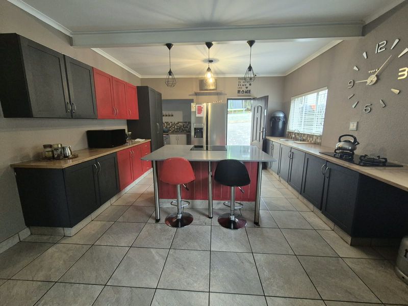 Spacious kitchen featuring a central island, contrasting dark and red cabinetry, tiled flooring, and integrated cooking facilities.