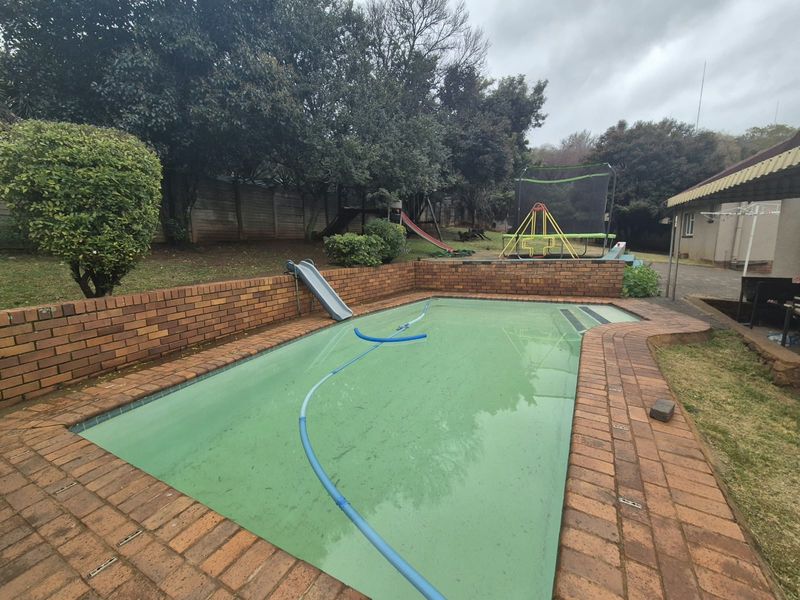 Outdoor pool area featuring a brick-lined swimming pool, paved surround, and established garden boundary.