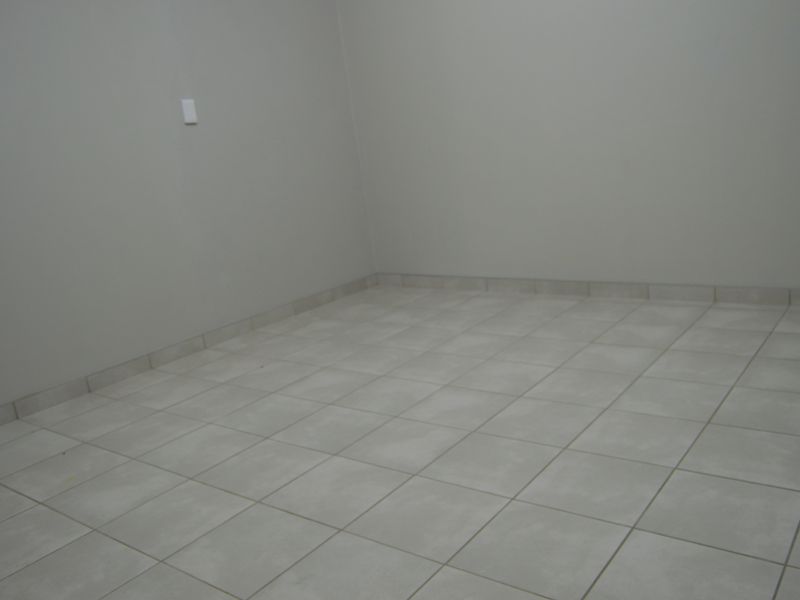 An empty room featuring neutral grey walls and light-colored ceramic floor tiles with matching tiled skirting.
