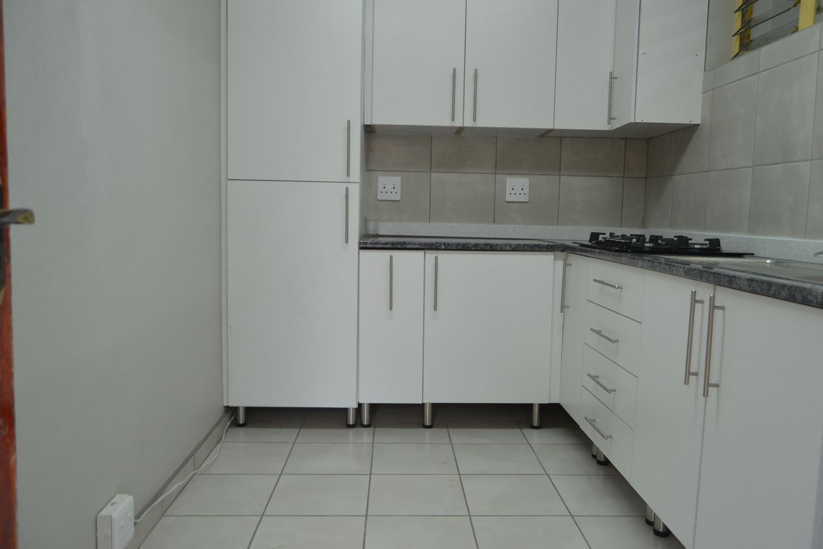 A clean, modern kitchen featuring white cabinetry, granite-look countertops, a gas hob, and neutral tiled flooring and backsplash.