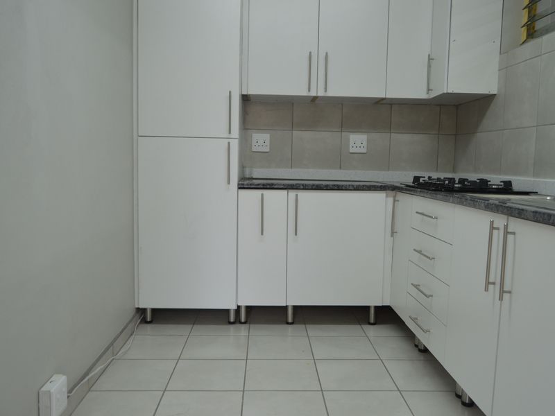 A clean, modern kitchen featuring white cabinetry, granite-look countertops, a gas hob, and neutral tiled flooring and backsplash.
