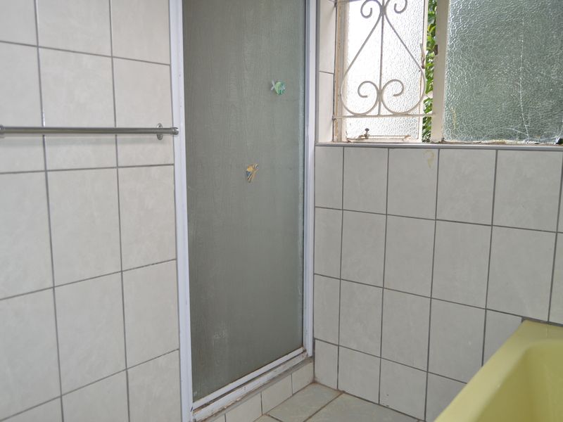A dated bathroom featuring tiled walls, a shower enclosure, and a bathtub, with a cracked window pane requiring repair.