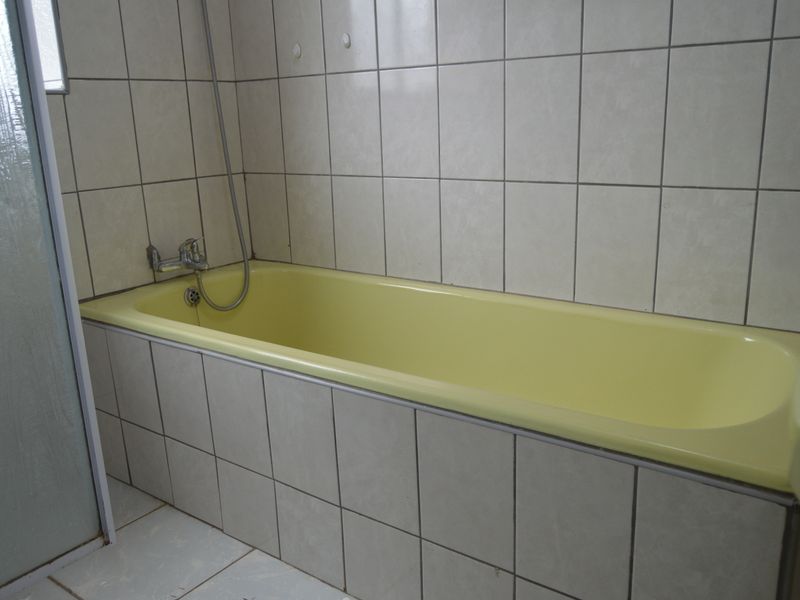 A dated bathroom featuring a yellow built-in bathtub with wall-mounted shower mixer and neutral ceramic tiling throughout.