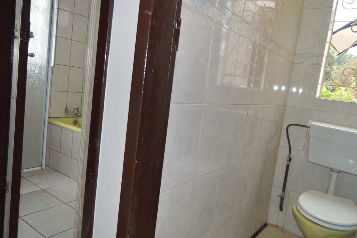 A functional bathroom featuring tiled walls and floors, a bathtub, shower enclosure, and a toilet with visible plumbing.
