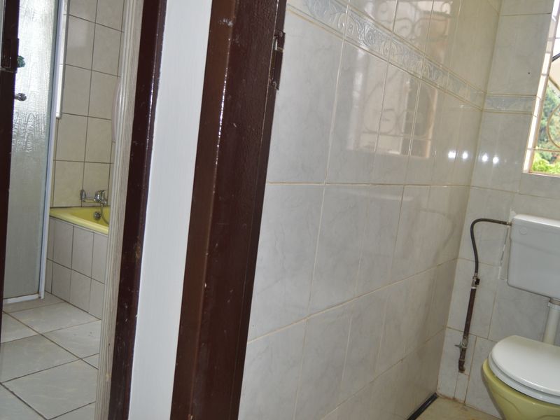 A functional bathroom featuring tiled walls and floors, a bathtub, shower enclosure, and a toilet with visible plumbing.