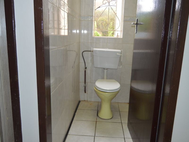 A compact, tiled bathroom featuring a standard toilet and a window with security bars, requiring cosmetic updates to improve its overall condition.