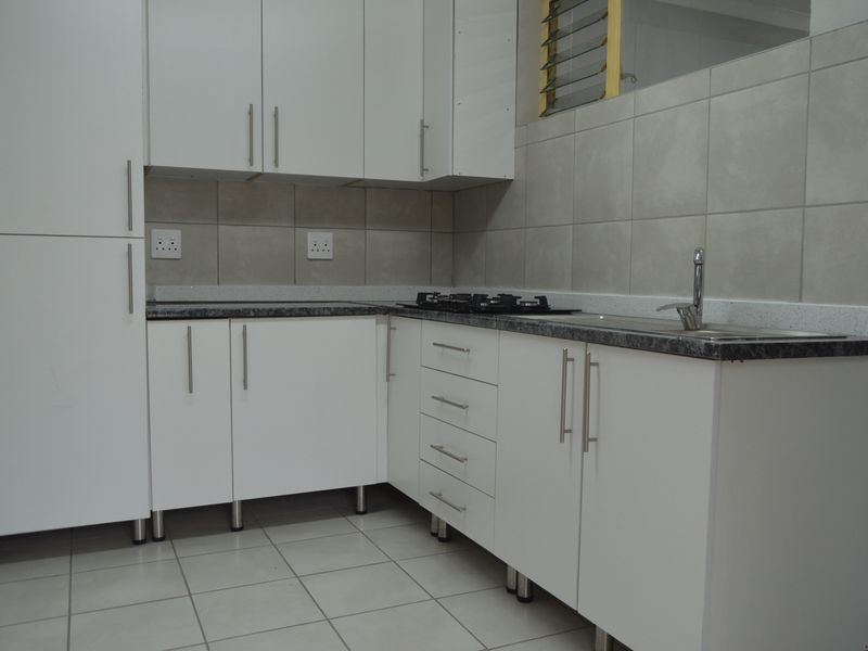 A clean, modern kitchen featuring white cabinetry, dark laminate countertops, a gas hob, and neutral tiled finishes throughout.