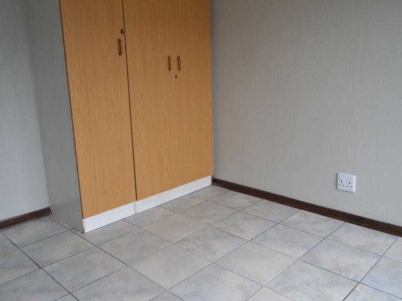 A simple, empty bedroom featuring tiled flooring and a built-in wooden wardrobe, providing a neutral canvas for potential interior design updates.