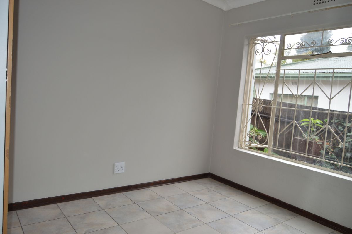 A clean, empty bedroom featuring neutral wall paint, tiled flooring, and a window fitted with decorative security burglar bars.