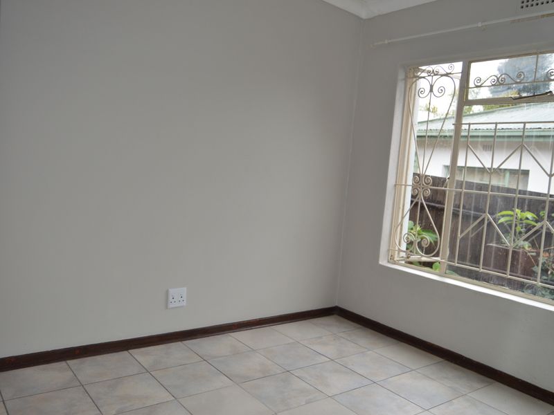 A clean, empty bedroom featuring neutral wall paint, tiled flooring, and a window fitted with decorative security burglar bars.