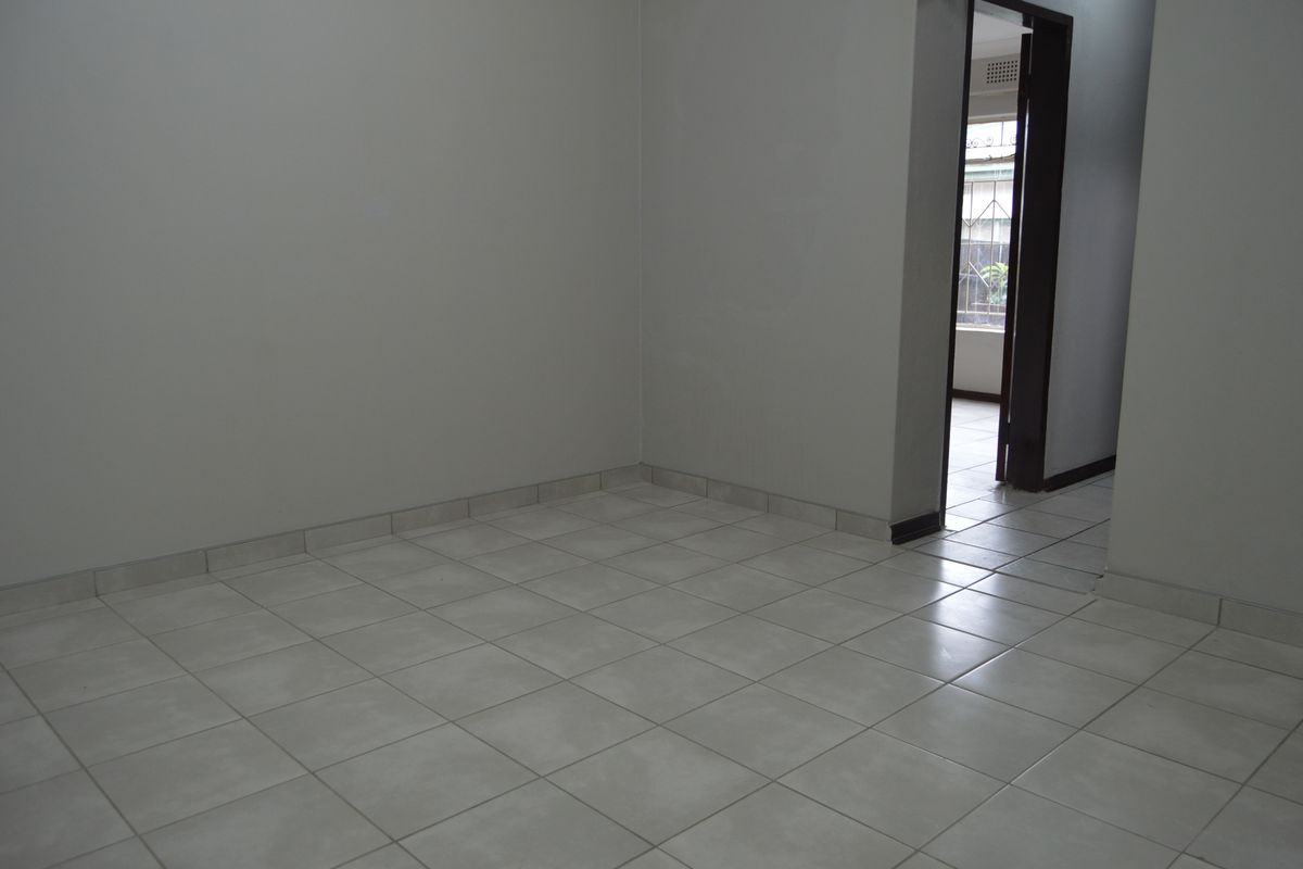 A vacant, neutral-toned living area featuring clean ceramic floor tiles and a doorway leading to an adjacent space.