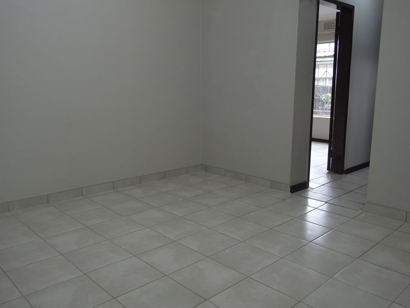 A vacant, neutral-toned living area featuring clean ceramic floor tiles and a doorway leading to an adjacent space.