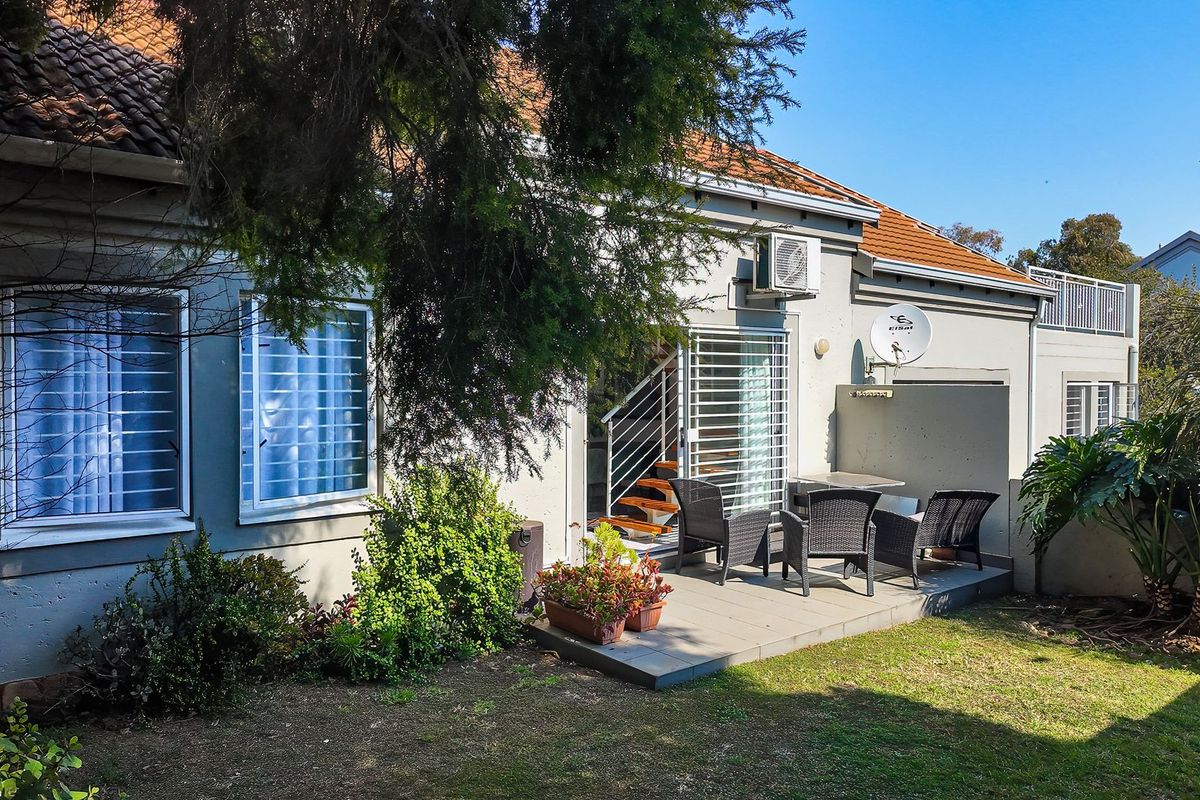 Rear exterior view of the townhouse featuring a paved patio area, security gates, and established garden space.