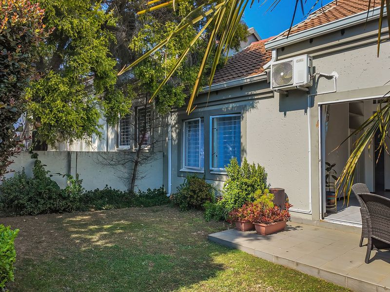 Rear view of the townhouse featuring a small tiled patio, a private garden area, and an exterior air conditioning unit mounted on the wall.