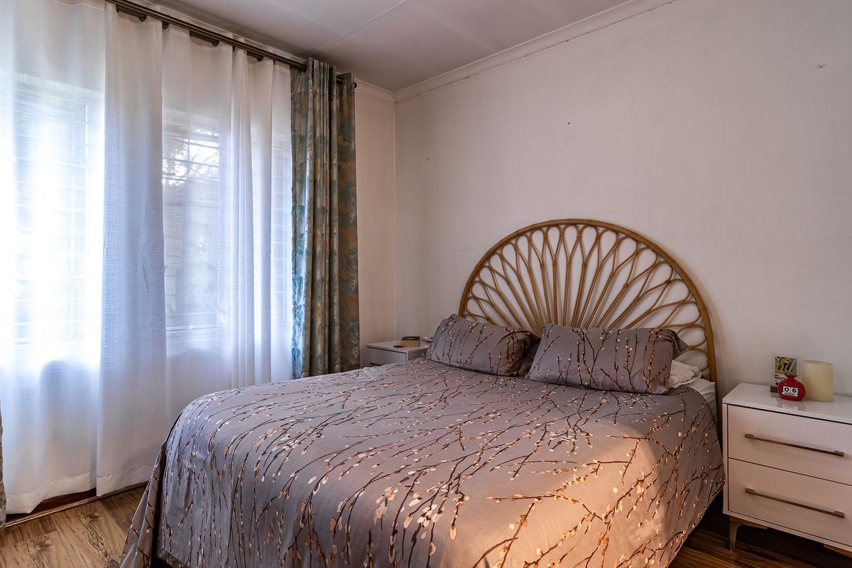 A bedroom featuring laminate flooring and natural light through a window with curtain rails.