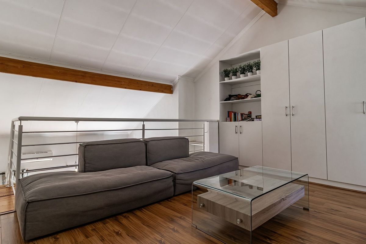 A cozy loft-style living area featuring vaulted ceilings with exposed timber beams, built-in storage cabinetry, and modern laminate flooring.