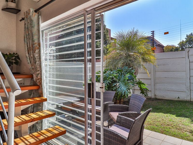 A view from the interior looking out onto a private patio area with tiled flooring, accessible via a sliding glass door with security gate.