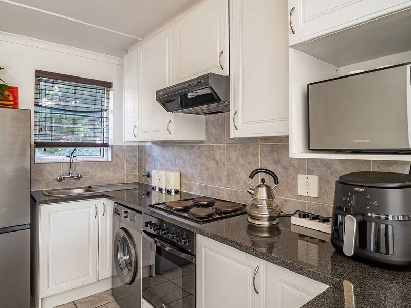 A functional kitchen featuring white cabinetry, granite countertops, a tiled backsplash, and integrated appliances including an oven, hob, and washing machine.