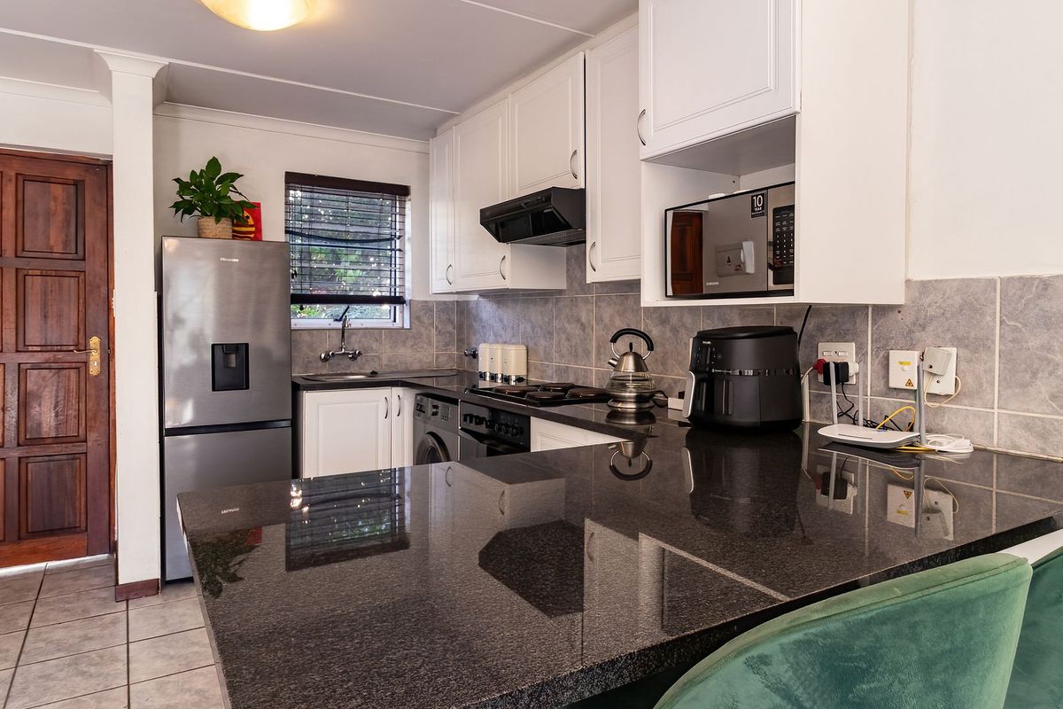 A functional kitchen featuring dark granite countertops, white cabinetry, a built-in oven with extractor fan, and tiled backsplash.