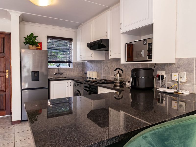 A functional kitchen featuring dark granite countertops, white cabinetry, a built-in oven with extractor fan, and tiled backsplash.