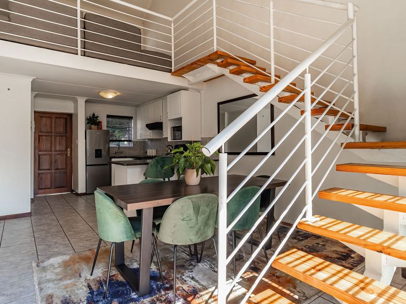 Open-plan living area featuring a mezzanine level, staircase with metal balustrade, and a functional kitchen with built-in cabinetry and tiled flooring.