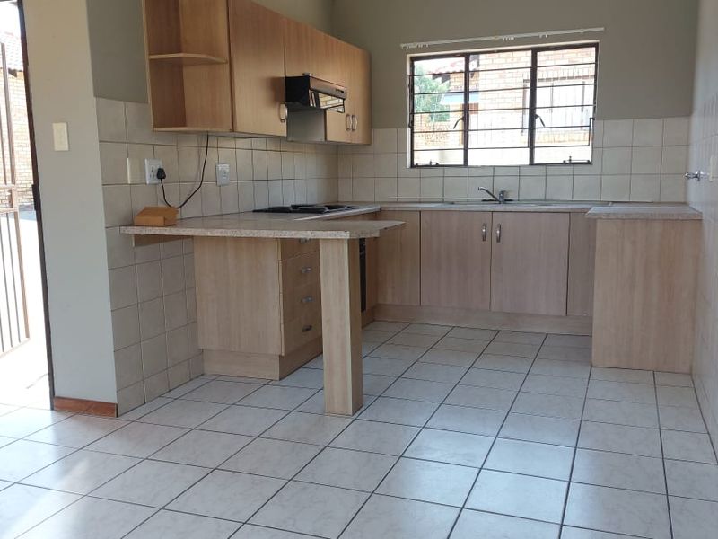 A functional kitchen featuring laminate cabinetry, tiled splashbacks, built-in hob with extractor, and tiled flooring, with direct access to the exterior.