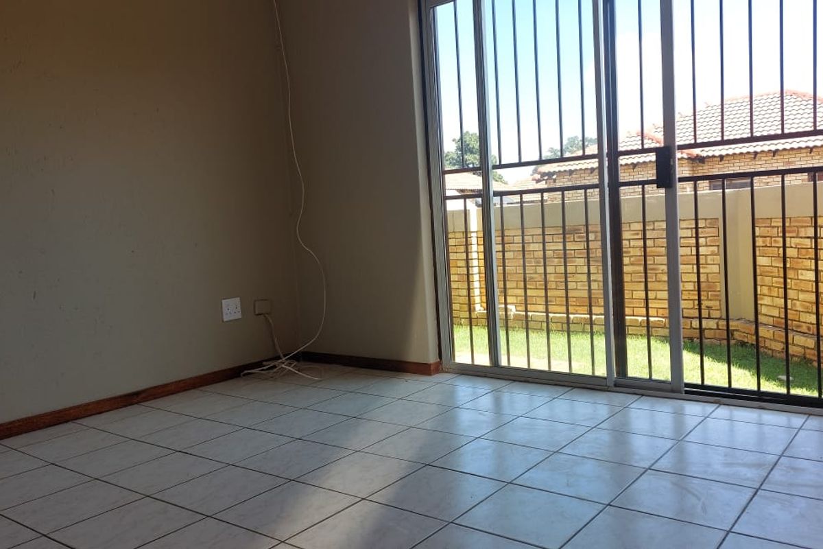 An empty living room featuring ceramic floor tiles and a sliding glass door with a security gate leading to the rear garden.