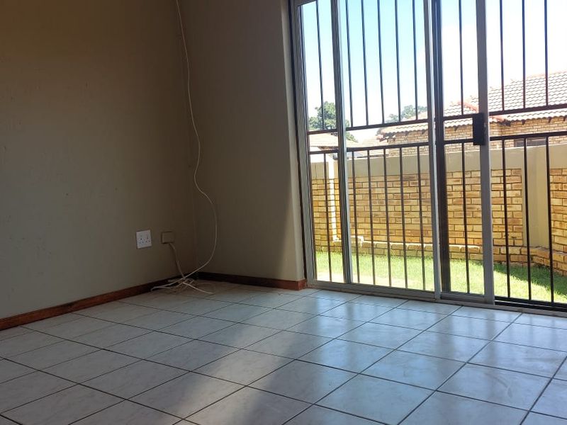 An empty living room featuring ceramic floor tiles and a sliding glass door with a security gate leading to the rear garden.